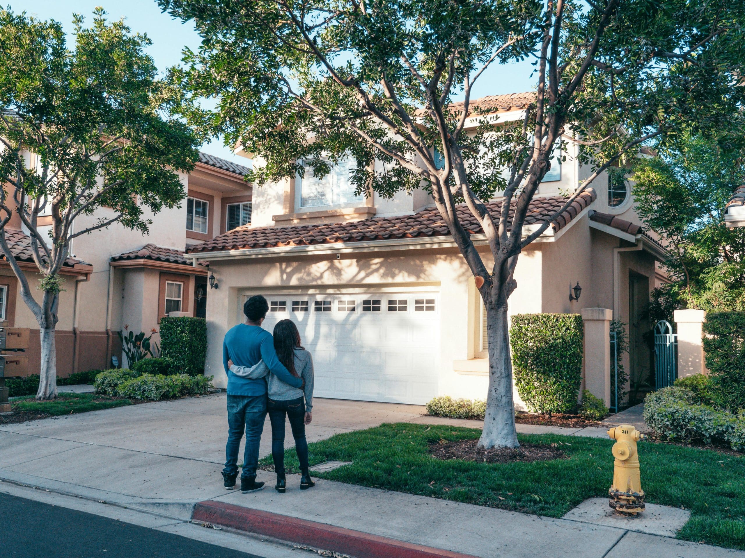 Mortgage Leads And Lists Couple hugging outside their newly purchased suburban home, showcasing togetherness and new beginnings.